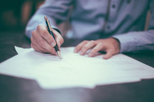 Man in business clothes at conference table holding a pen and signing his name to a document