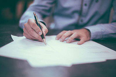 Man at a desk holding a pen and signing his name to a document