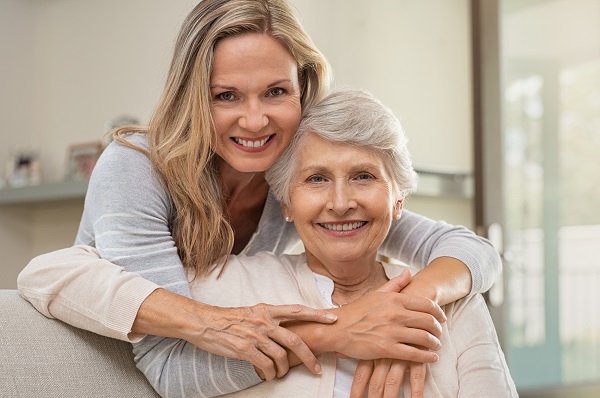 Cheerful mature woman embracing senior mother at home and looking at camera..