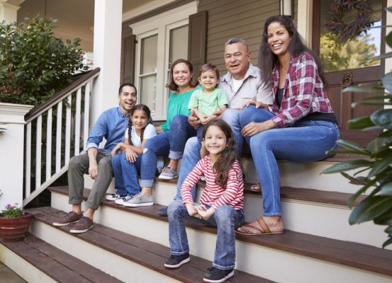 Multi Generation Family Sit On Steps Leading Up To House Porch