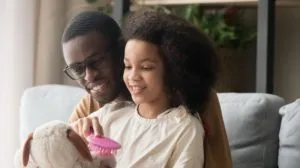 Father and young daughter at home on a couch playing with a stuffed animal