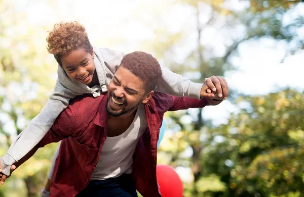 True moment of happiness. Happy child flying and piggyback. Father holding his daughter on shoulders and laughing.