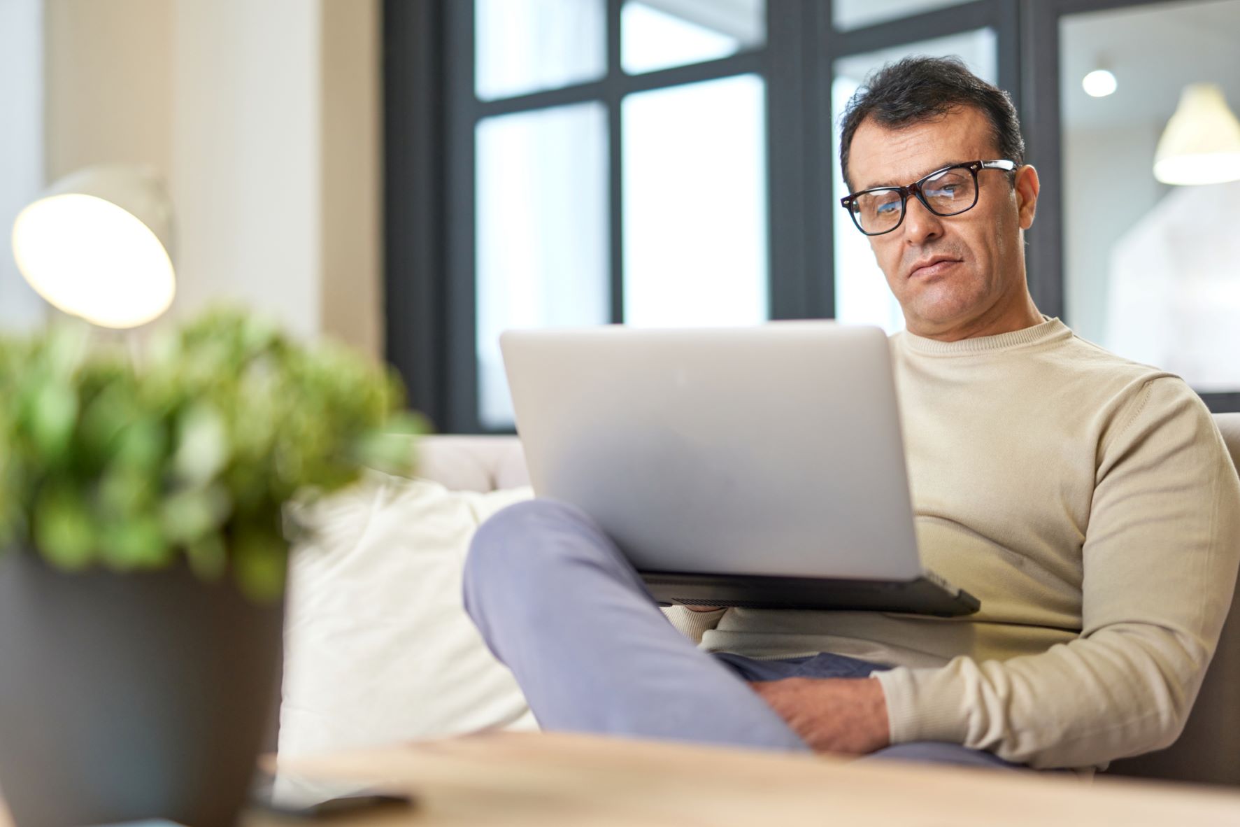 Mature man sittin at home on a sofa and reading on his laptop