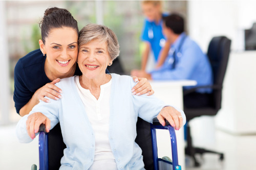 senior woman in a wheel chair with a nurse behind her, both happy and smiling
