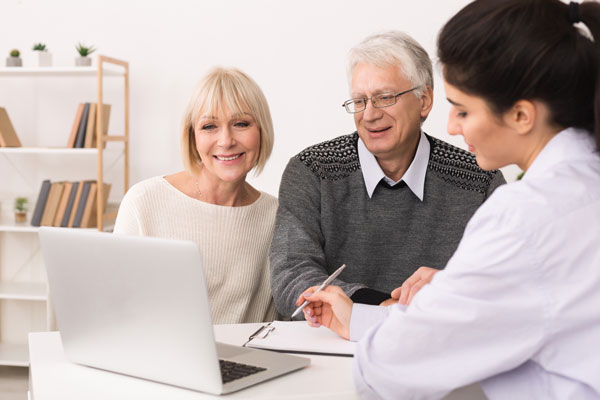 Mature man and woman meeting with doctor, looking over documents with an open computer laptop nearby