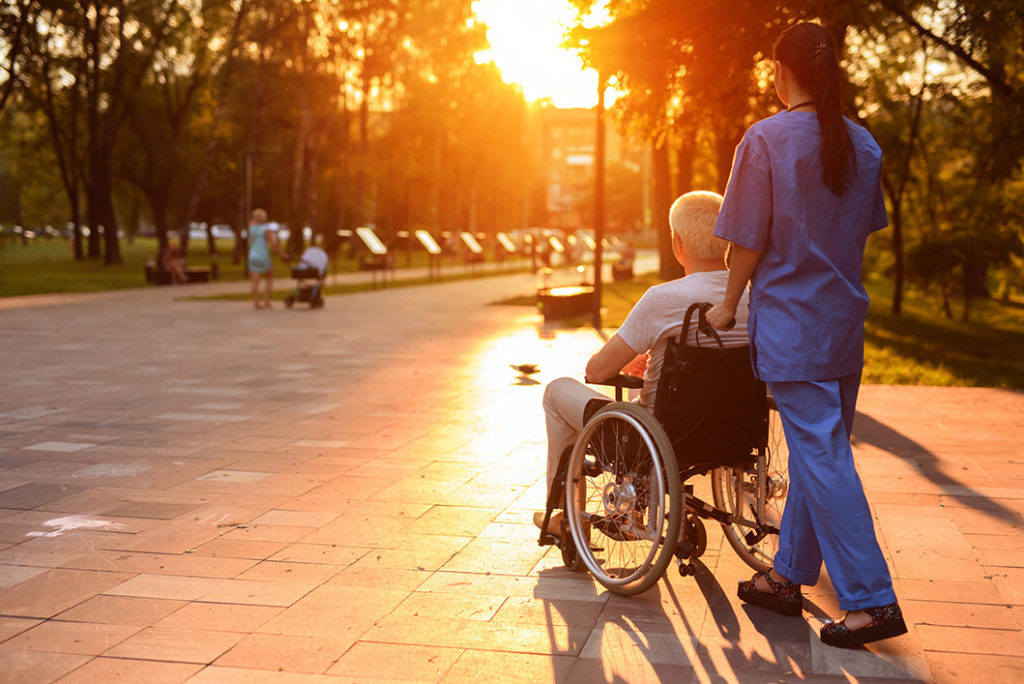 What a beautiful sunset. An old man in a wheelchair and a nurse are walking in the park at sunset