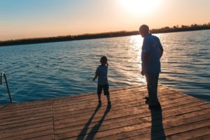 Grandfather with grandson enjoying time together by the lake. Boy trowing rock in water.