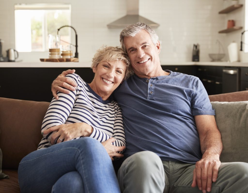 Mature couple in their home on the couch, smiling at the camera