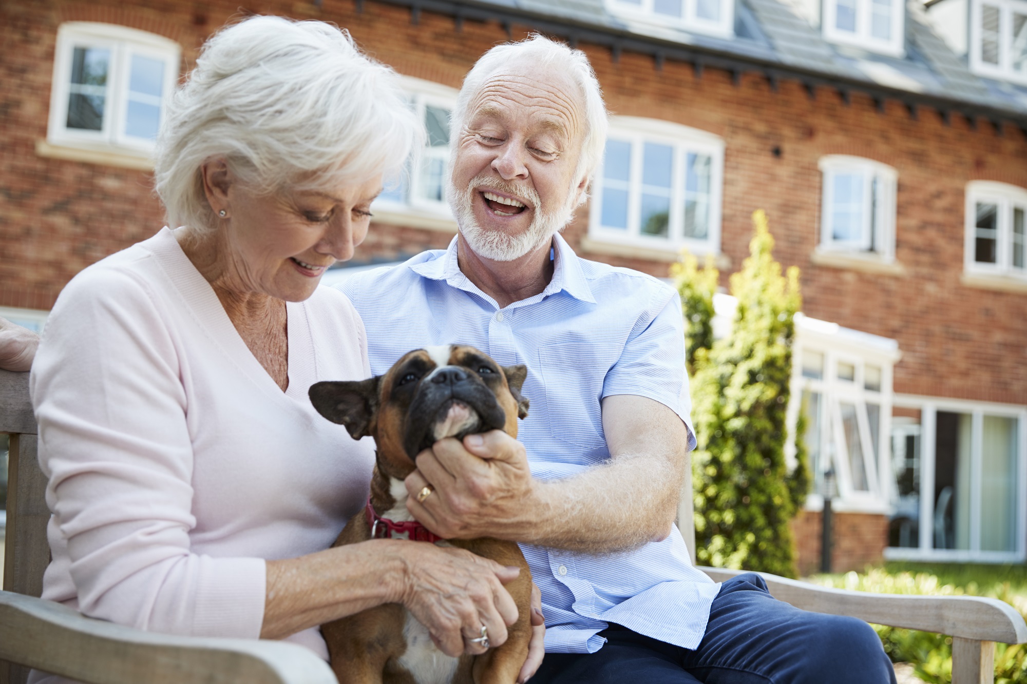 Happy senior woman and man with their dog sitting outside an assisted living facility