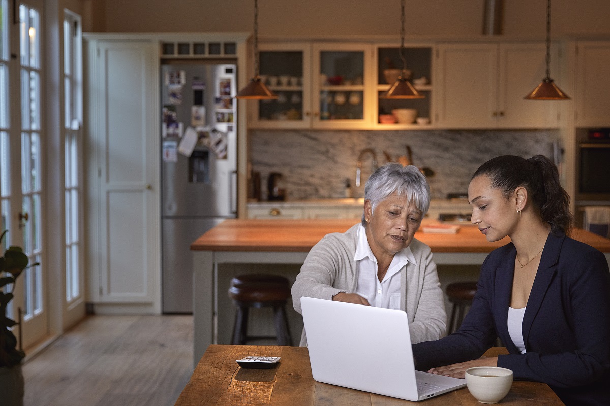 Adult woman with senior mother working together on their estate plans using a laptop in the kitchen