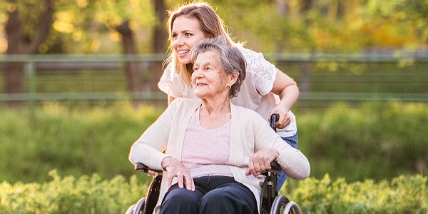 Elderly grandmother in wheelchair with an adult granddaughter outside in spring nature