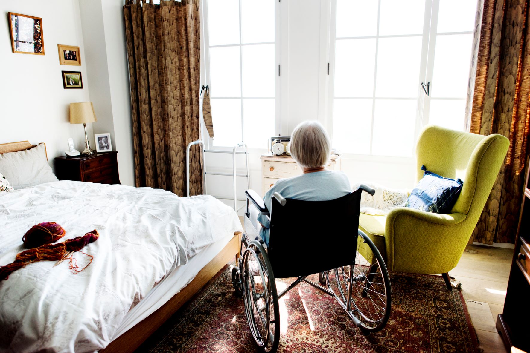 Senior woman in a wheel chair looking out a window of her bedroom